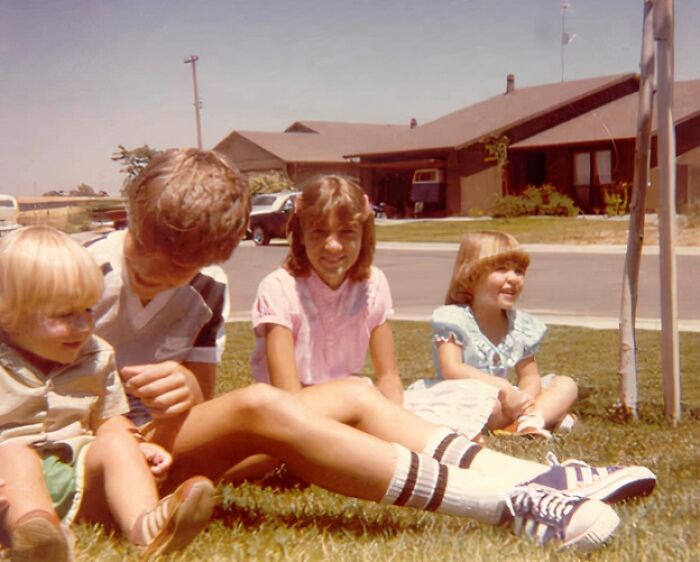 Four kids sitting on grass outside a suburban home, capturing a hilariously awkward childhood moment.