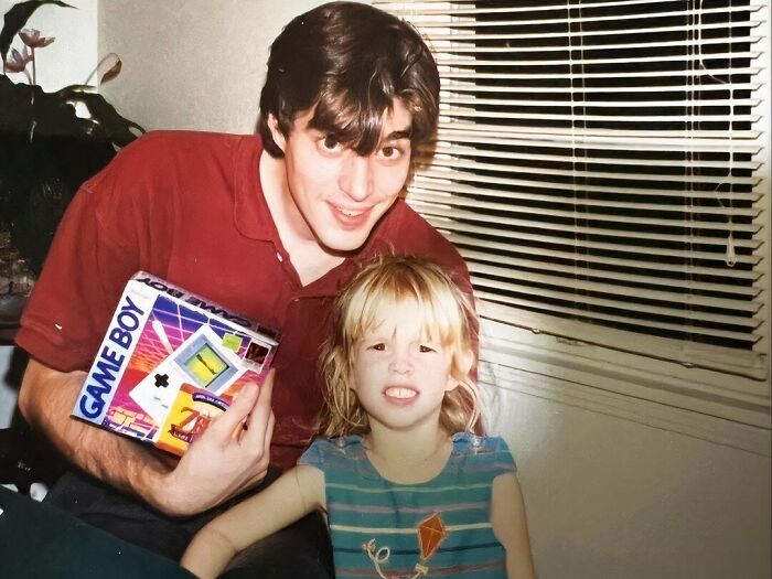 Young man and child smiling awkwardly with vintage Game Boy box, showcasing hilariously awkward childhood pics.