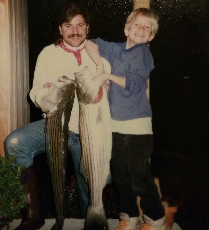 Man and boy holding two large fish in a childhood photo capturing a hilariously awkward moment outdoors at night.