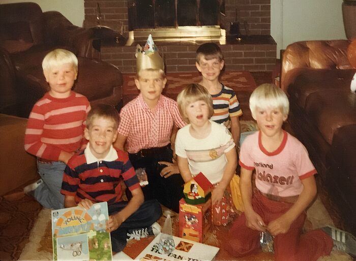 Group of six children in retro clothing sitting indoors with birthday hats and gifts, a hilarious awkward childhood pic.