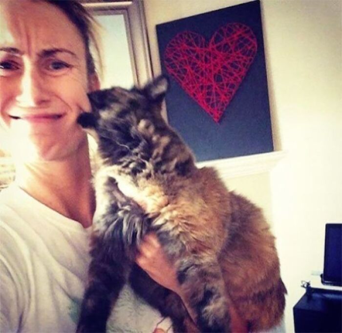 Woman making a funny regret face while holding a large cat, capturing a humorous regret moment at home.