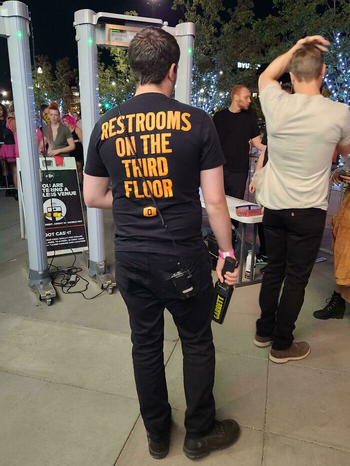 Security guard wearing a clever shirt to direct people to restrooms, showcasing a genius idea for solving annoying problems.