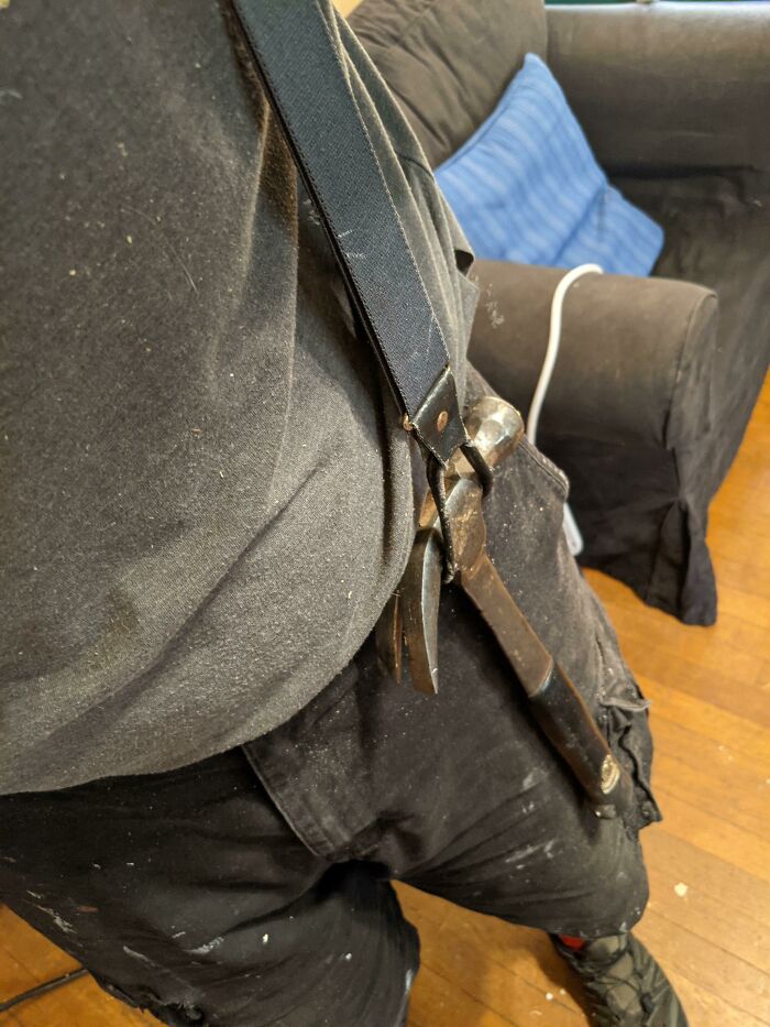 Using a hammer attached to suspenders as a hands-free tool holder for a genius problem-solving idea.