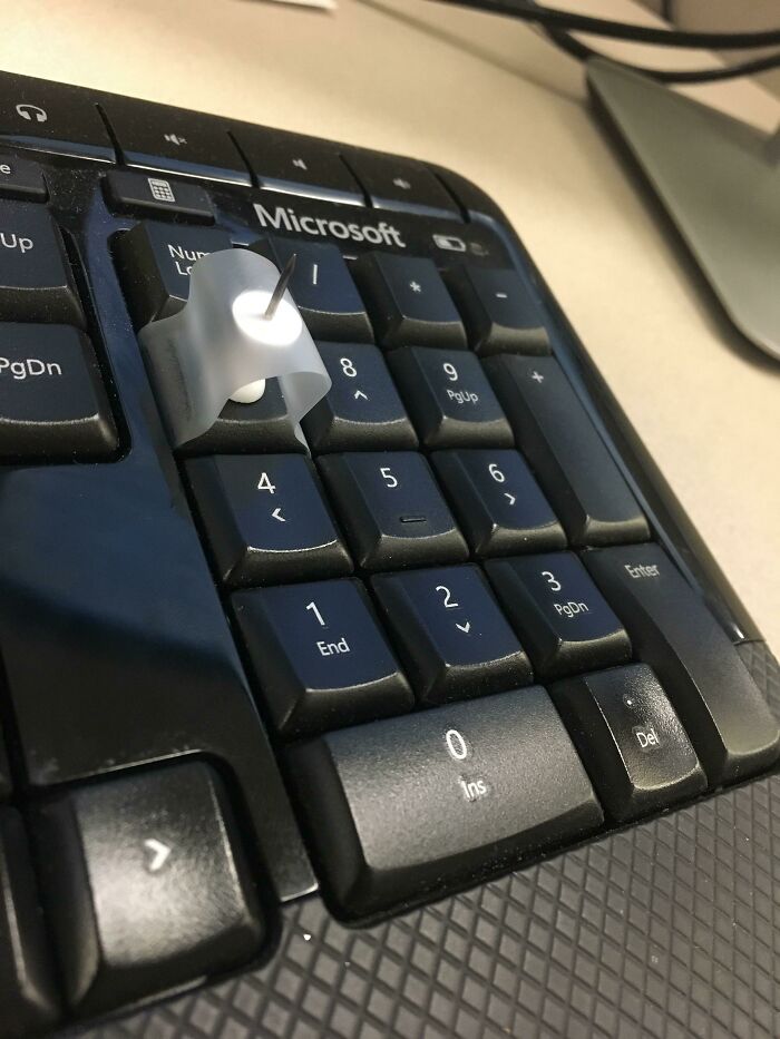 Keyboard with a pushpin held by a plastic cap on a key demonstrating creative problem solving and genius ideas.