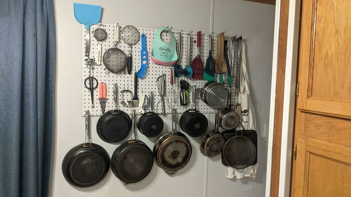 Kitchen tools and pans organized neatly on a wall-mounted pegboard, showcasing genius ideas to solve annoying problems.