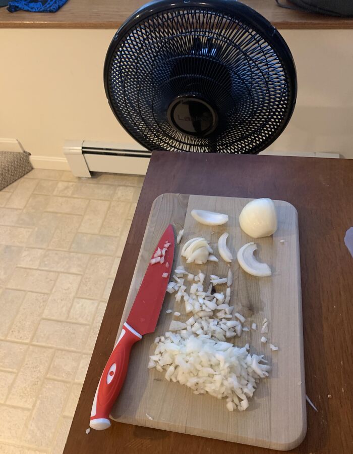 Kitchen hack showing a fan blowing away onion smell while chopping on a cutting board with a red knife.