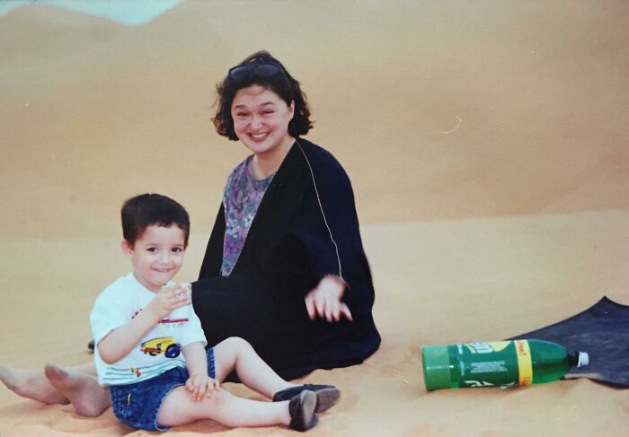 Young child and woman sitting on sand, captured in a funny and awkward childhood moment photo.