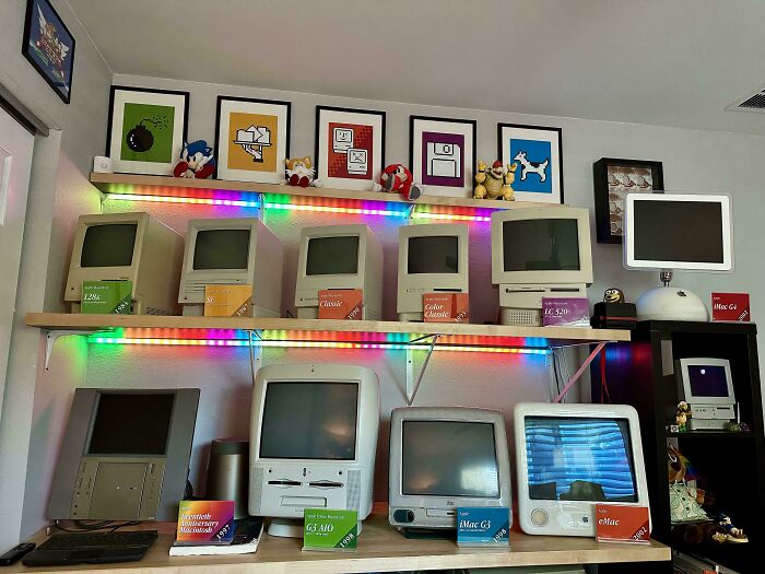 Collection of vintage Apple computers displayed on shelves with colorful LED lights, showcasing a tech obsession collection.
