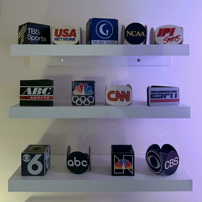 Collection of vintage TV microphone flags featuring various sports and news networks displayed on white shelves.