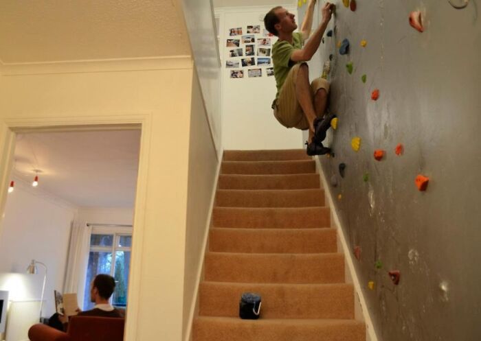 Man climbing an indoor rock wall beside stairs, demonstrating a creative and genius problem-solving idea at home.