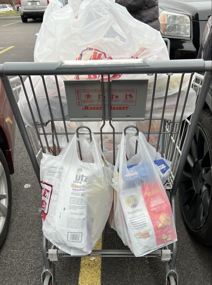 Grocery bags hung from a shopping cart handle to prevent items from touching the ground, a clever problem-solving idea.