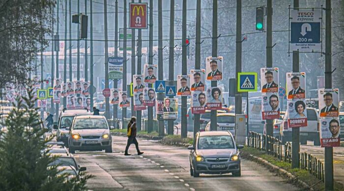 Urban street lined with numerous political campaign posters on poles and passing cars