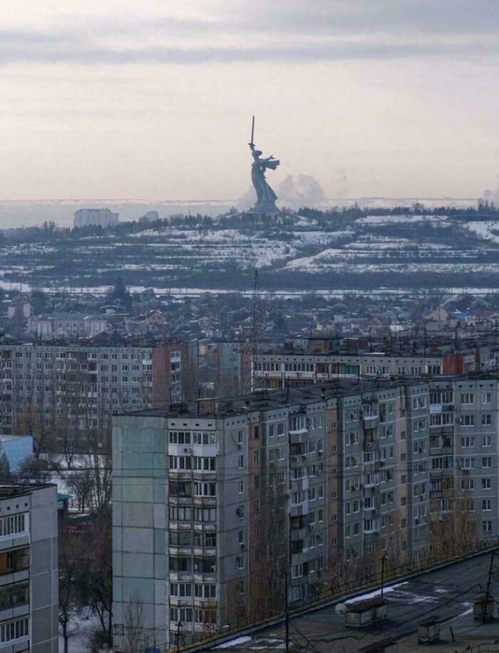 Gloomy cityscape with old apartment buildings and a giant statue on snowy hills