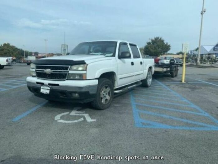 White pickup truck improperly parked across multiple handicap spots in a parking lot, showing poor judgment and brain capacity.