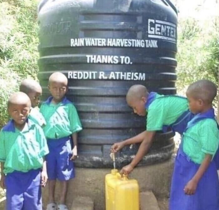 Several kids in green and blue uniforms gather around a rainwater harvesting tank with an unusual donation message.