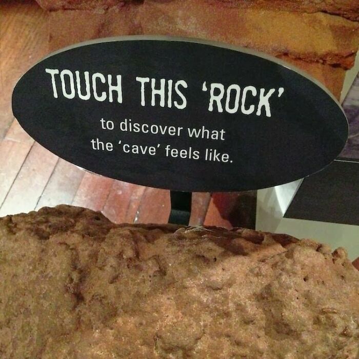 Sign with suspicious quotation marks saying "Touch this 'rock' to discover what the 'cave' feels like" on display.