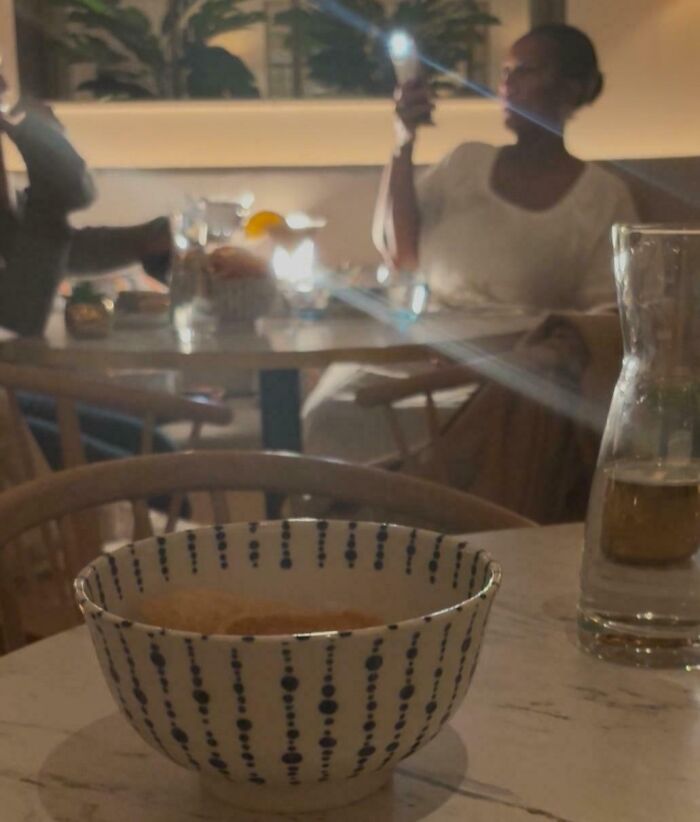 Woman influencer taking a photo with phone flash on in a dim restaurant setting, highlighting cringy influencer behavior.