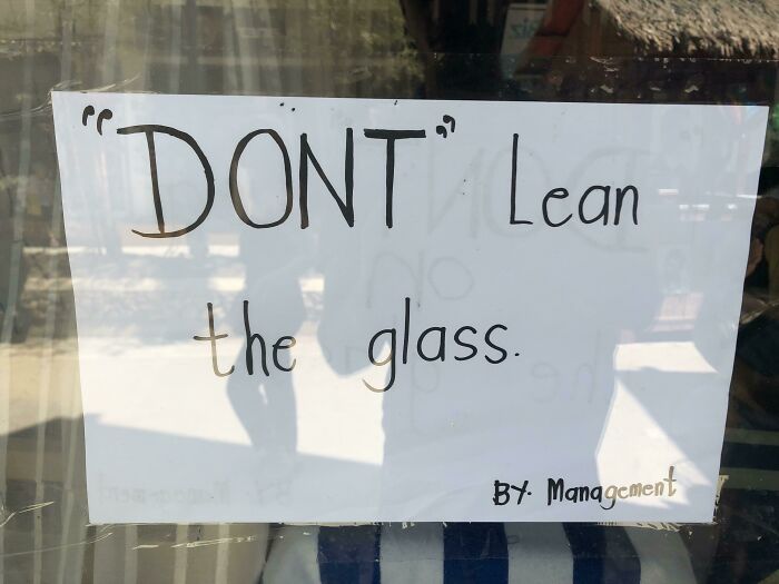 Hilariously suspicious sign with quotation marks around "DONT" warning not to lean the glass, showing quirky punctuation.