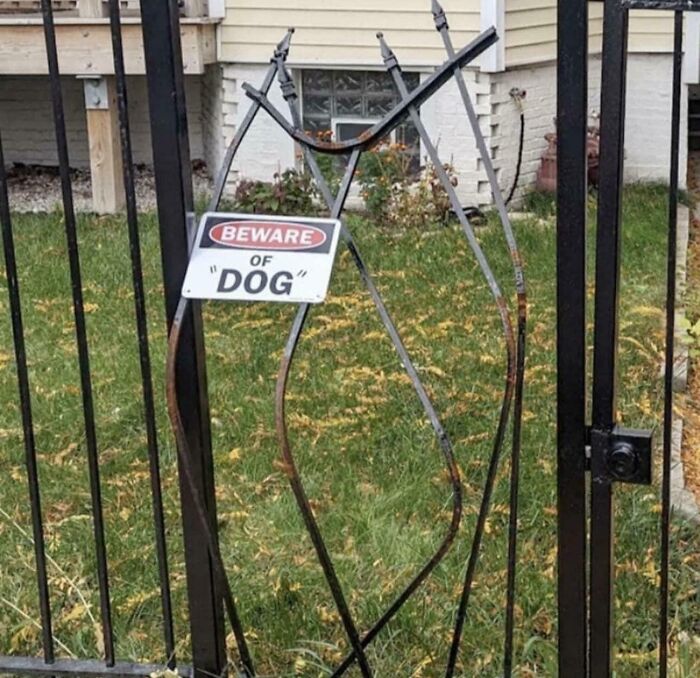 A metal gate with a sign humorously warning about a suspicious dog using quotation marks on the word dog.
