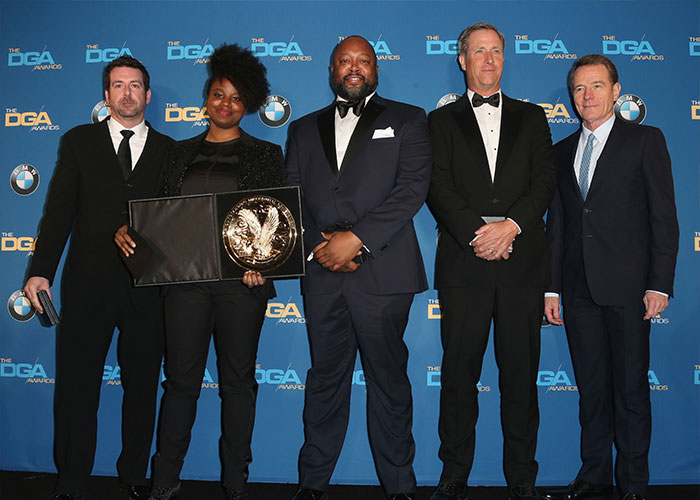 Five formally dressed individuals posing at the DGA Awards event with an award, highlighting Hollywood connection.