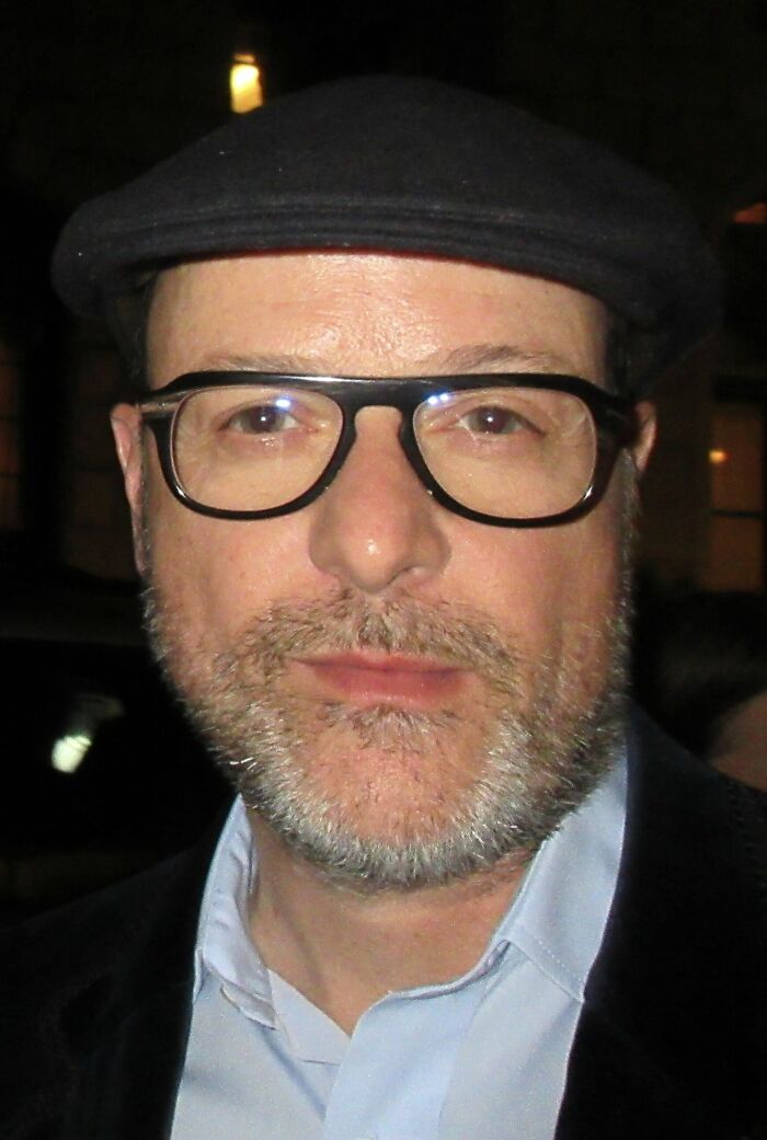 Matthew Vaughn wearing a black cap and glasses, posing for a close-up portrait at a nighttime event.