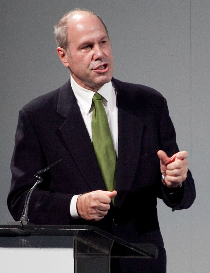 Michael Eisner speaking at a podium, wearing a black suit and green tie, highlighting key moments in his career.
