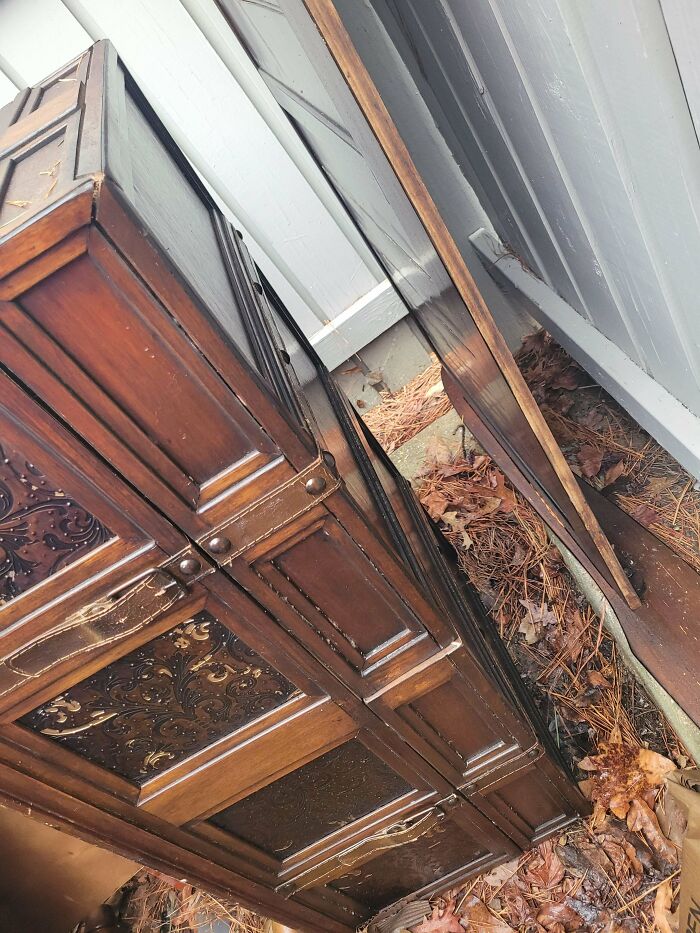 An ornate, dark wood cabinet sitting outside, a valuable item found while dumpster diving.