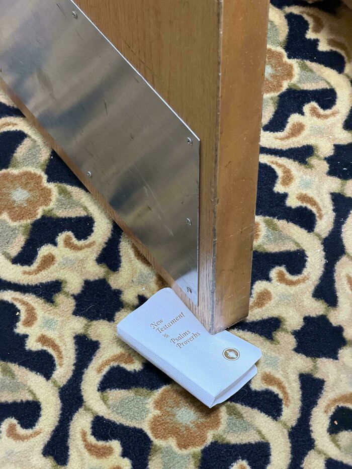 A tiny New Testament book used as a doorstop against a wooden pew, among interesting pictures.