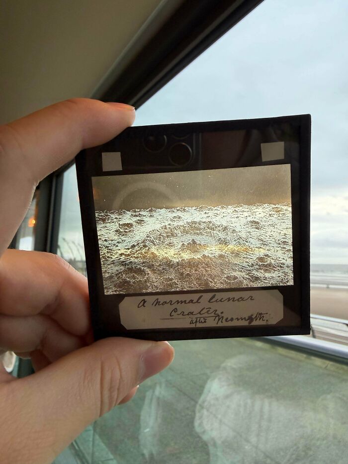 A hand holds a vintage glass slide with an image of a textured surface, a remarkable antique discovery.