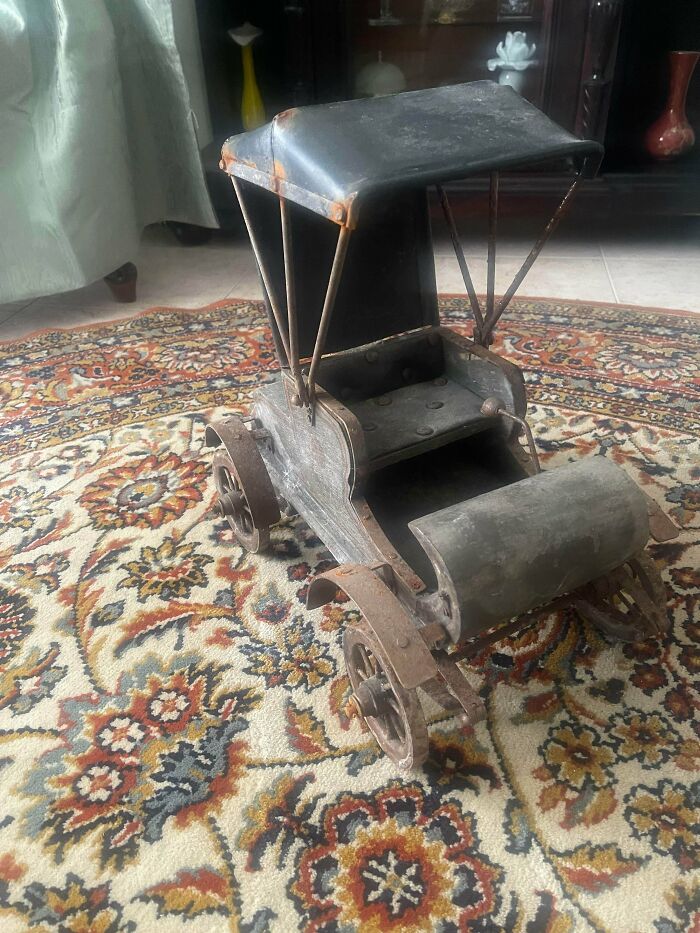 A remarkable antique model car with an open top sits on a patterned rug, highlighting a special find.