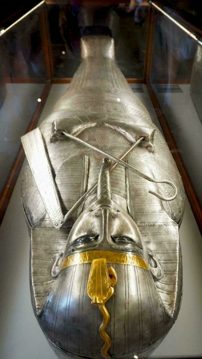Silver Egyptian mummy case displayed in a museum glass case, showcasing ancient historical finds