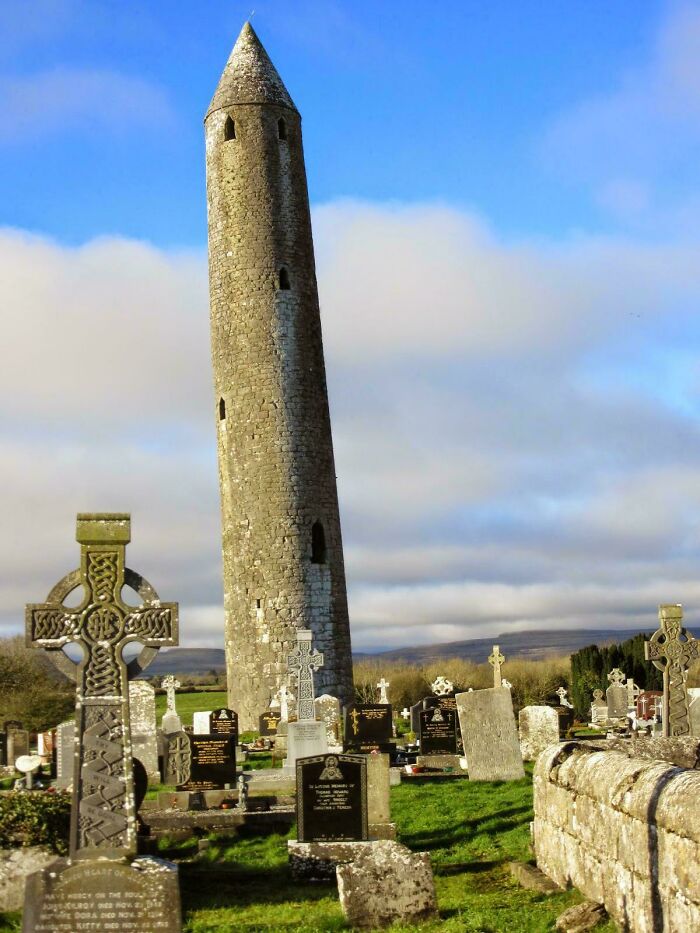 Tall ancient stone round tower standing in a cemetery, among remarkable historical finds from Ireland.