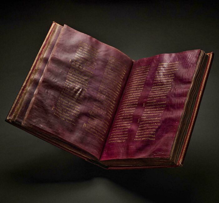 An open ancient manuscript with purple parchment and gold lettering, showcasing historical finds.