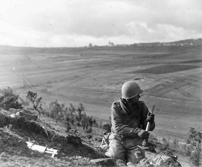 A soldier in a helmet kneeling in a field with a weapon, part of emotional historical photos.