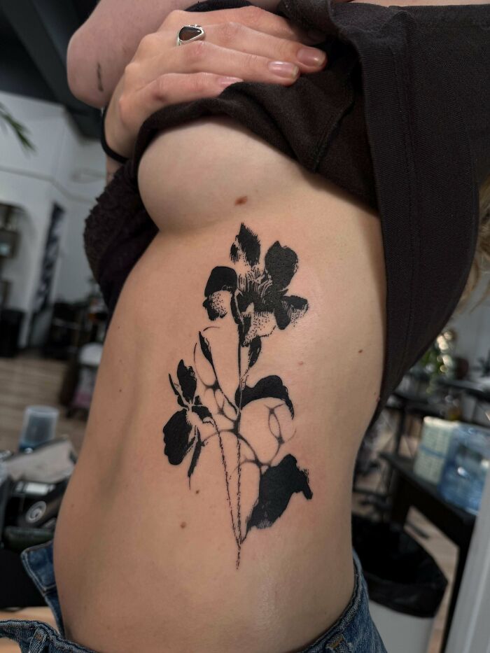A person displays a stunning black silhouette tattoo of flowers on their side, a happy and permanent piece of body art.