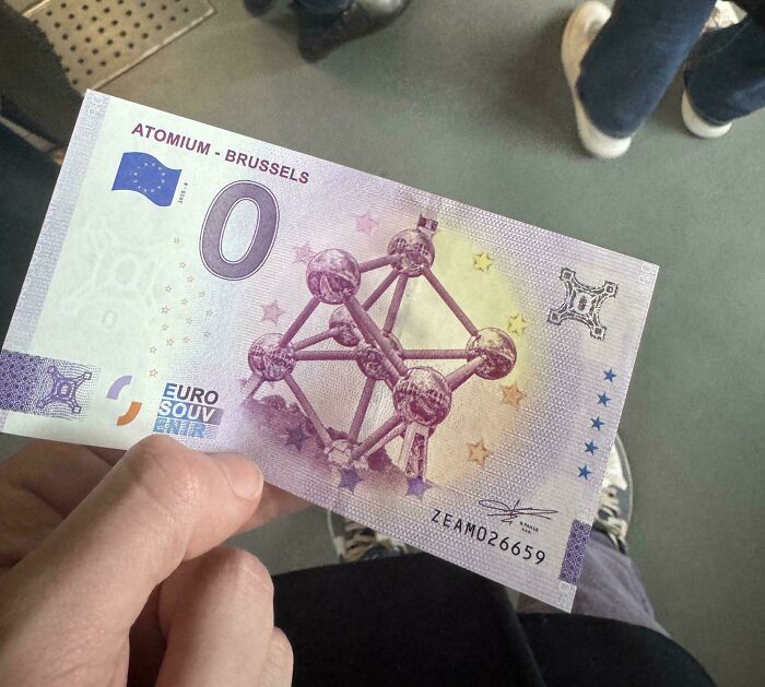 A peculiar 0 Euro souvenir banknote featuring the Atomium, a landmark in Brussels, held in a person's hand.