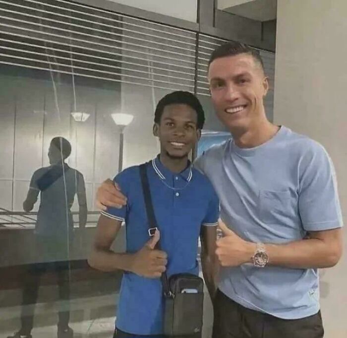 A peculiar moment captured in real life of a fan smiling and giving a thumbs up next to soccer player Cristiano Ronaldo.