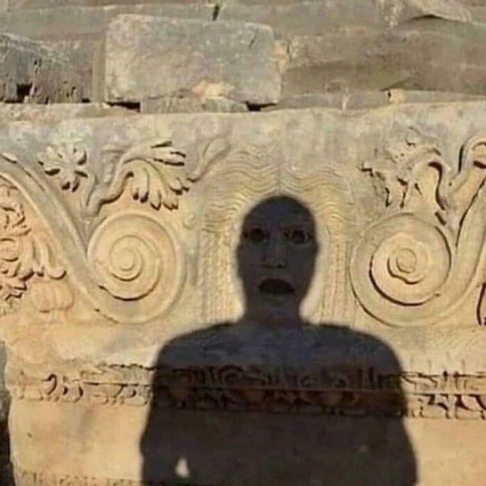 A peculiar shadow with a surprised face projected onto an ancient, ornate stone carving, an interesting thing spotted in real life.