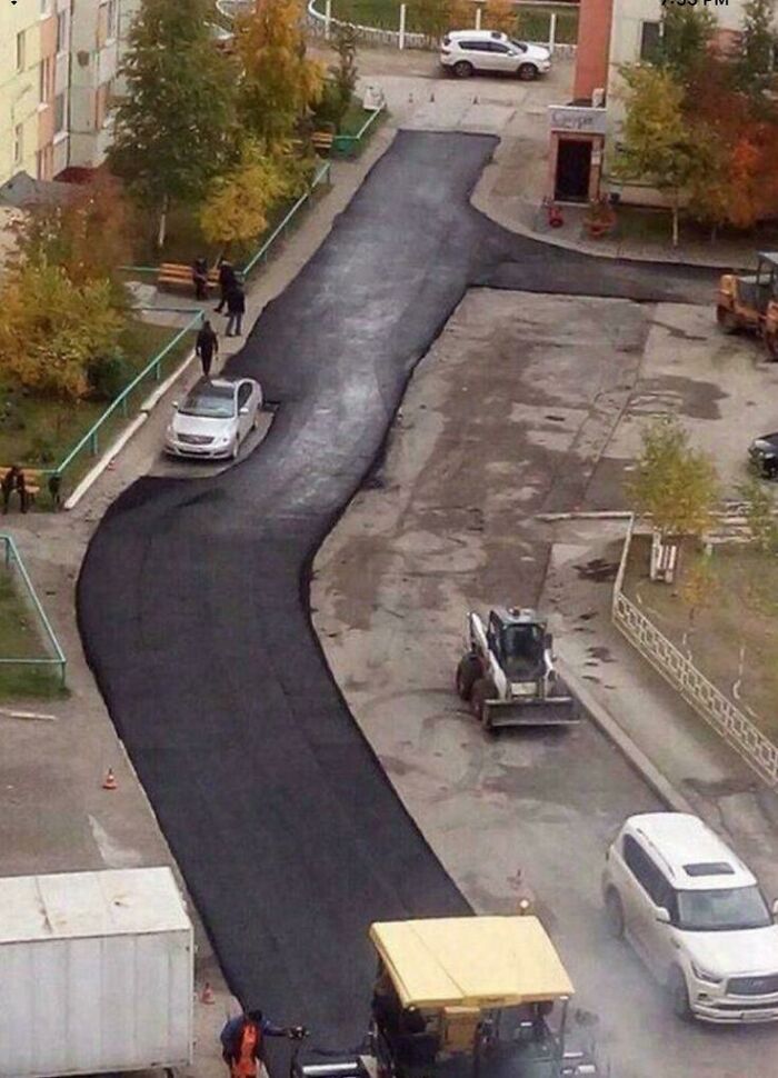 An aerial view of a peculiar, irregularly paved road in a residential area, with vehicles and construction equipment. Spotted in real life.