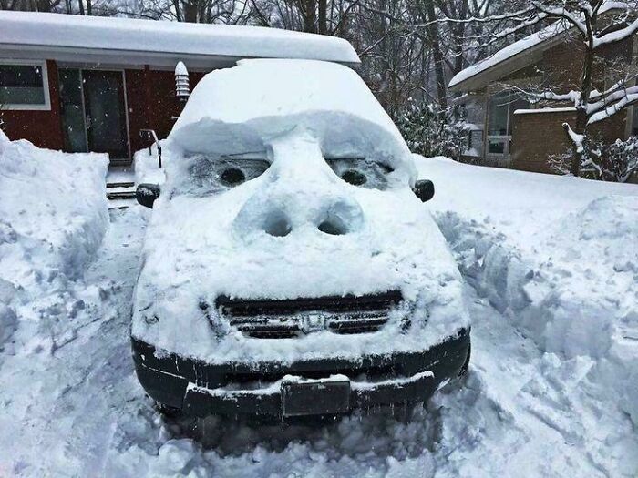 A peculiar thing: a car covered in snow, sculpted to resemble a large face with a prominent nose.
