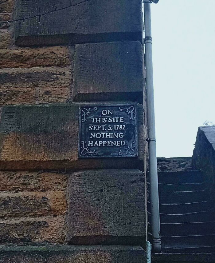 A metal plaque on a stone wall reads On This Site Sept. 5, 1782 Nothing Happened for the Not Interesting community.