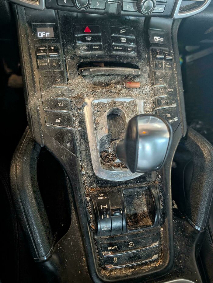 Car mechanics deal with an extremely dirty car interior, covered in debris and grime around the gear shift.
