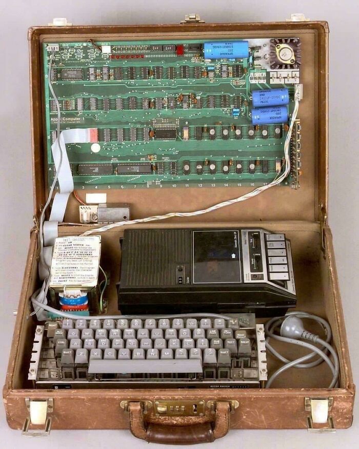 An open briefcase revealing an Apple I computer, including a circuit board, keyboard, and cassette player, a historical photo from days we will never experience.