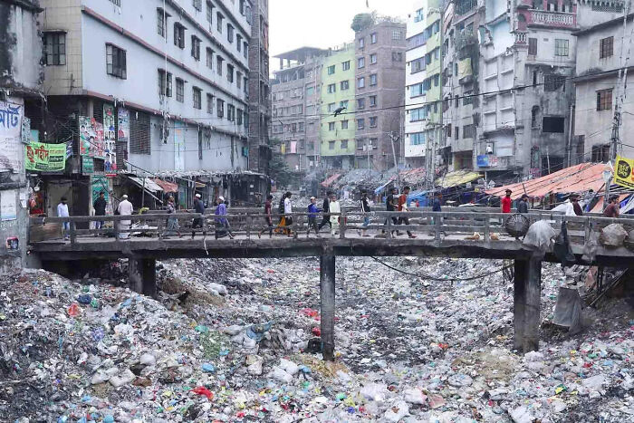 Crowded bridge over trash-filled river in urban hell area