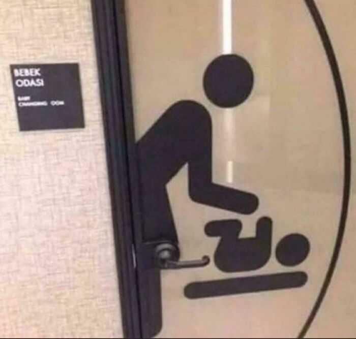 A changing room sign depicting an adult changing a baby, but the door handle is awkwardly placed on the baby's head, a funny fail.