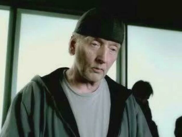 An older man with a thin face and dark beanie looking downward, wearing a grey hoodie over a light shirt, highlighting nonsensical movie details.