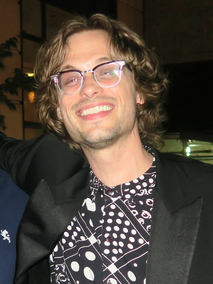 Matthew Gray Gubler smiling, wearing glasses and a patterned shirt, captured in a casual nightlife setting for career highlights.
