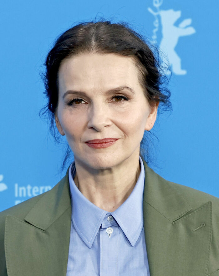 Juliette Binoche at a film festival event, wearing a blue shirt and green blazer, showcasing her bio and career highlights.