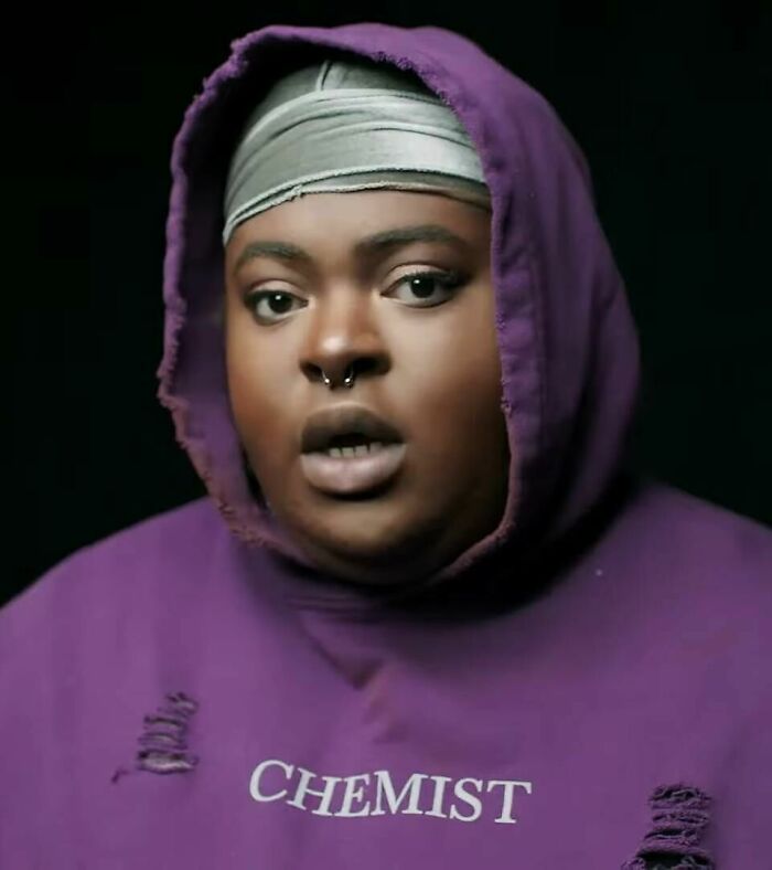 Chika wearing a purple hooded sweatshirt and headband, with a focused expression in a dark background.