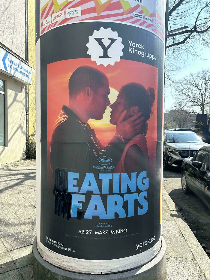 Movie poster vandalized with black paint altering the text, an example of mild vandalism on an urban street pillar.